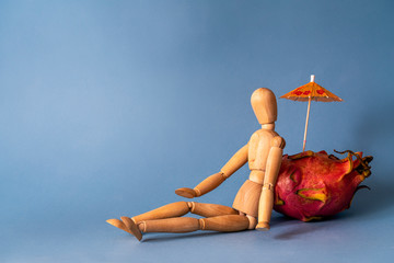 Wooden man enjoys relaxing next to pitaya fruit. Tropical vacation concept
