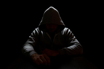 A man in a hood sits in the dark with arms extended forward. Crime and Internet Security