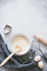 Bakery ingredients-wheat flour, raw eggs and kitchen utensils on a gray stone backgound
