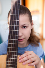 Portrait of teenage girl guitarist with fretboard of guitar, looking at camera