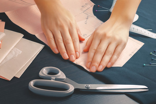 Close up of the hands of a young seamstress girl who attached one of the patterns to the edge of the fabric using a sewing pin.