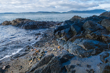 Landscape of dark rocks and the Pacific Ocean with distant islands at Washington Park in Anacortes, Washington