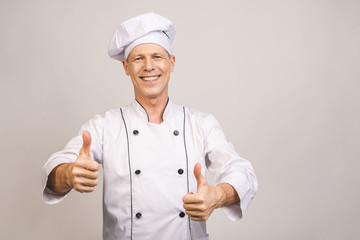 Senior handsome chef cook isolated on grey background. Thumbs up.