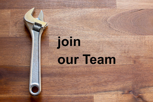 a flexible chromed.adjustable wrench lies on a dark wooden table. The solgan join our team is written on the table in black letters