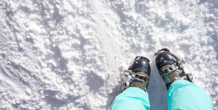 Top view of foot in ski boots and light green pants. The concept of sport and recreation. Copy space, snow background