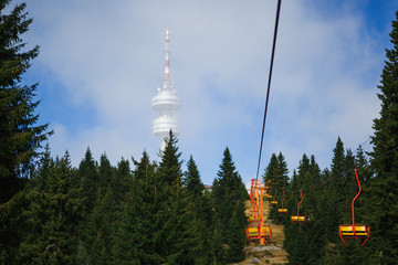 Cable car in the ski area of Bulgaria in summer. Yellow chair ski lift is among the green firs and...