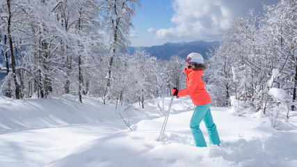 Young female skier in bright jacket stands and looks at the scenic mountain landscape. The concept of sport and recreation. space for text, back view