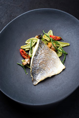 Gourmet fried Italian gilthead fish filet with spinach pasta, glasswort and tomatoes as closeup on a modern design plate