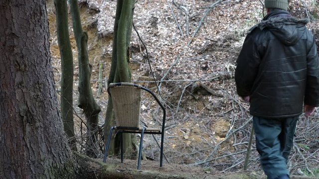 Man sits on chair under tree in the wood and observe environment - (4K)