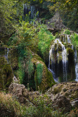 Fototapeta na wymiar Streams of the waterfall fall from the rock and sparkle in the sun among the greenery. Attractions of Bulgaria - Krushuna waterfalls and mountain trail in Smolyan