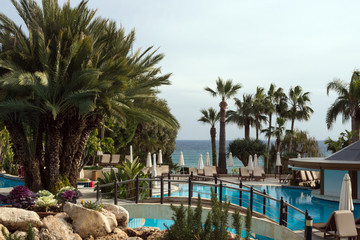 Blue pool, palm trees, umbrellas and the sea in the distance. Waiting for rest.