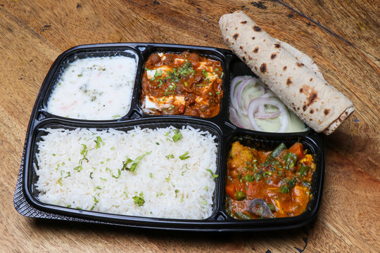 Indian food thali with rice chapati kadai paneer, mix vegetable, raita & onion rings, in disposable tray