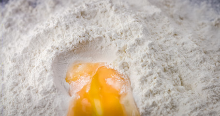 Egg falls on white flour. Ingredients for making fresh bread or pasta