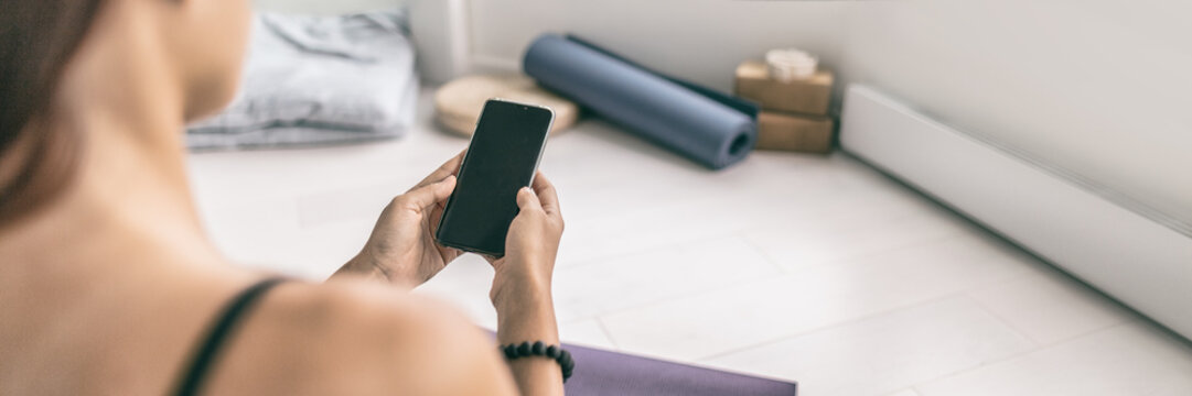 Phone woman using mobile app on fitness class at gym or yoga studio strength training workout in apartment looking at cellphone screen panoramic banner.