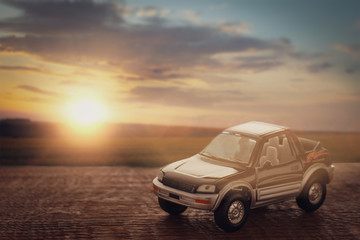 Fototapeta na wymiar Toy car on a background of grass and sunset sky: the concept of road travel and car insurance