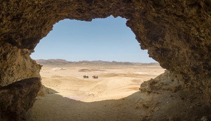 A look from the cave at two ATVs in the desert against the backdrop of the mountains on a hot sunny day