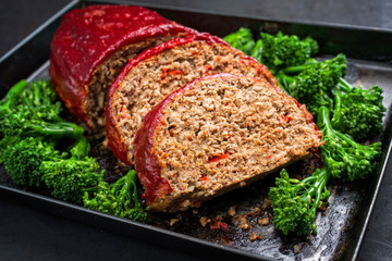 Traditional American meatloaf from ground beef with ketchup and broccoli as closeup on a rustic...