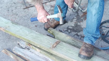 Slow motion of older man hammering nails on old wood during a diy project at home