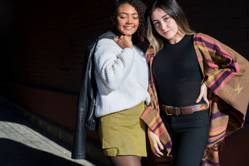 Portrait of two beautiful fashionable Hispanic girls, happy smiling posing for the camera. Autumn street art photo. Y, Z