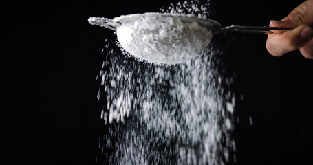 Cook hands sifting flour or sugar by sieve on black background