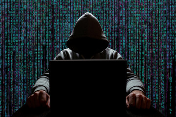 unknown computer hacker in front of a laptop on a background of binary code