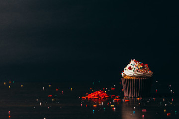 Cupcake sprinkled with decorations on a black background.