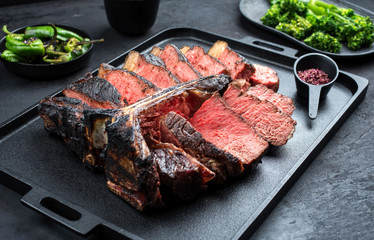 Barbecue dry aged wagyu porterhouse beef steak sliced with large fillet piece with hot chili and rapini broccoli rabe as closeup on a modern design black cast iron tray