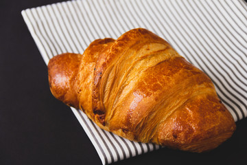 Rosy croissant on white napkin on black background.