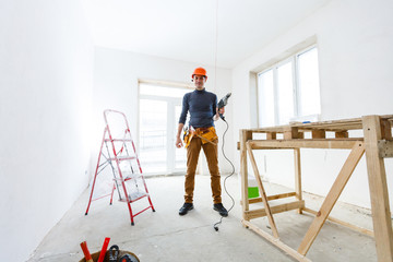 The builder in a protective helmet holds the professional puncher-hammer with a drill of the big...