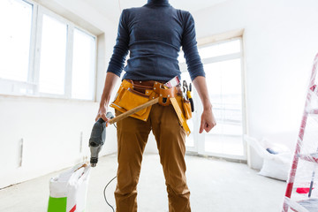 The builder in a protective helmet holds the professional puncher-hammer with a drill of the big...