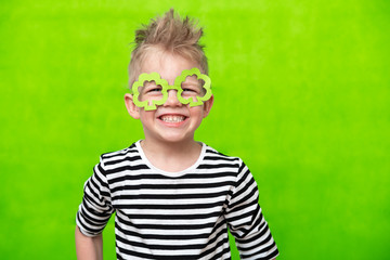 portrait little smiling caucasian boy in mask of leprechaun shamrock clover glasses for irish St....