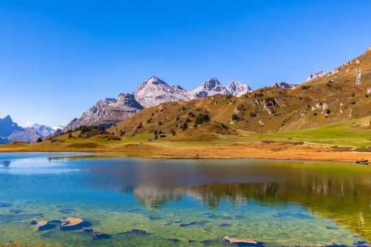 Stunning panorama view of lake Lai da Vons and the Swiss Alps on sunny day in golden autumn with clear blue sky in background, Canton of Grisons, Switzerland.