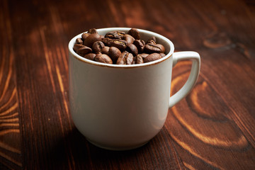 A coffee cup filled with fresh arabica coffee beans on a burnt wooden background.
