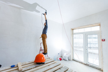 Builder worker with pneumatic hammer drill perforator equipment making hole in wall at construction...