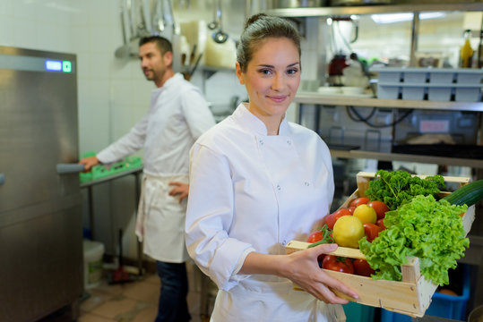 female chef showing crate of fresh fruit and vegetables