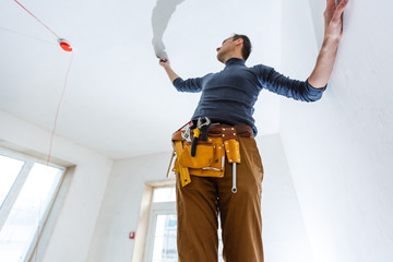 Thirty years old manual worker with wall plastering tools inside a house. Plasterer renovating...