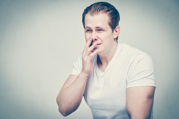 A man in a white T-shirt suffers from sinusitis. Toned.