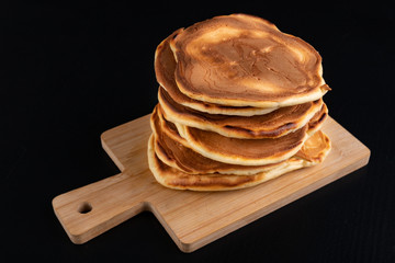 Pile of fresh pancakes on a wooden board. Tasty cookies on the kitchen table.