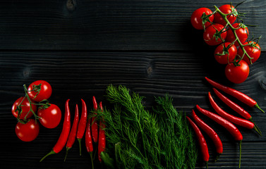 Cherry tomatoes, chilli and fresh herbs on a black wooden background