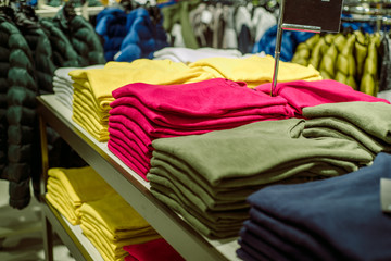 Sweaters in the store.Stack of folded knitted. Yellow green and purple jacket. women's clothing stacked on the heels of the store.