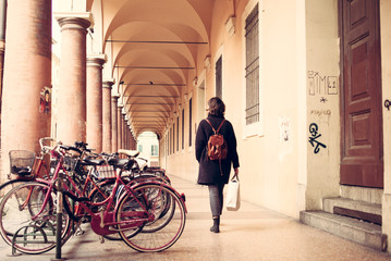 Woman walking next to vintage bikes under Bologna porticoes covered footpath in the  historical medieval centre of Bologna. Emilia-Romagna, Italy. - 324057474