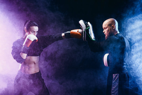 Woman exercising with trainer at boxing and self defense lesson, studio, smoke on background.
