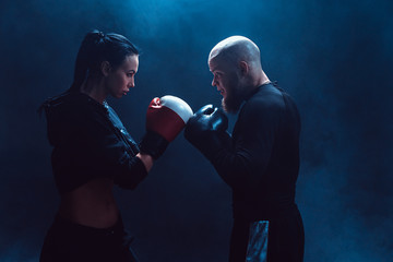 Woman exercising with trainer at boxing and self defense lesson, studio, smoke on background....