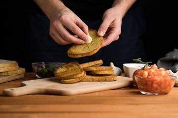 Hands rubbing garlic on a grilled slice of bread preparing an Italian bruschetta snack dark background