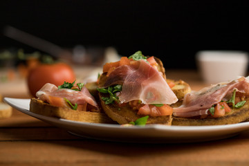 Bruschetta with tomato, basil, garlic and Italian ham on a white plate surrounded by ingredients,...