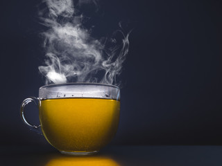 Glass cup with hot tea. Steam on a dark background.