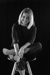 beautiful girl in black clothes and glasses sits on a wooden chair in studio