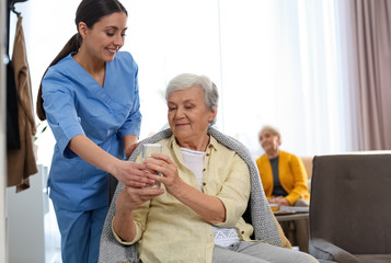 Care worker giving water to elderly woman in geriatric hospice