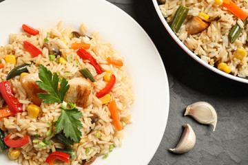 Delicious rice pilaf with chicken and vegetables on black table, closeup