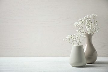 Gypsophila flowers in vases on table against light background. Space for text